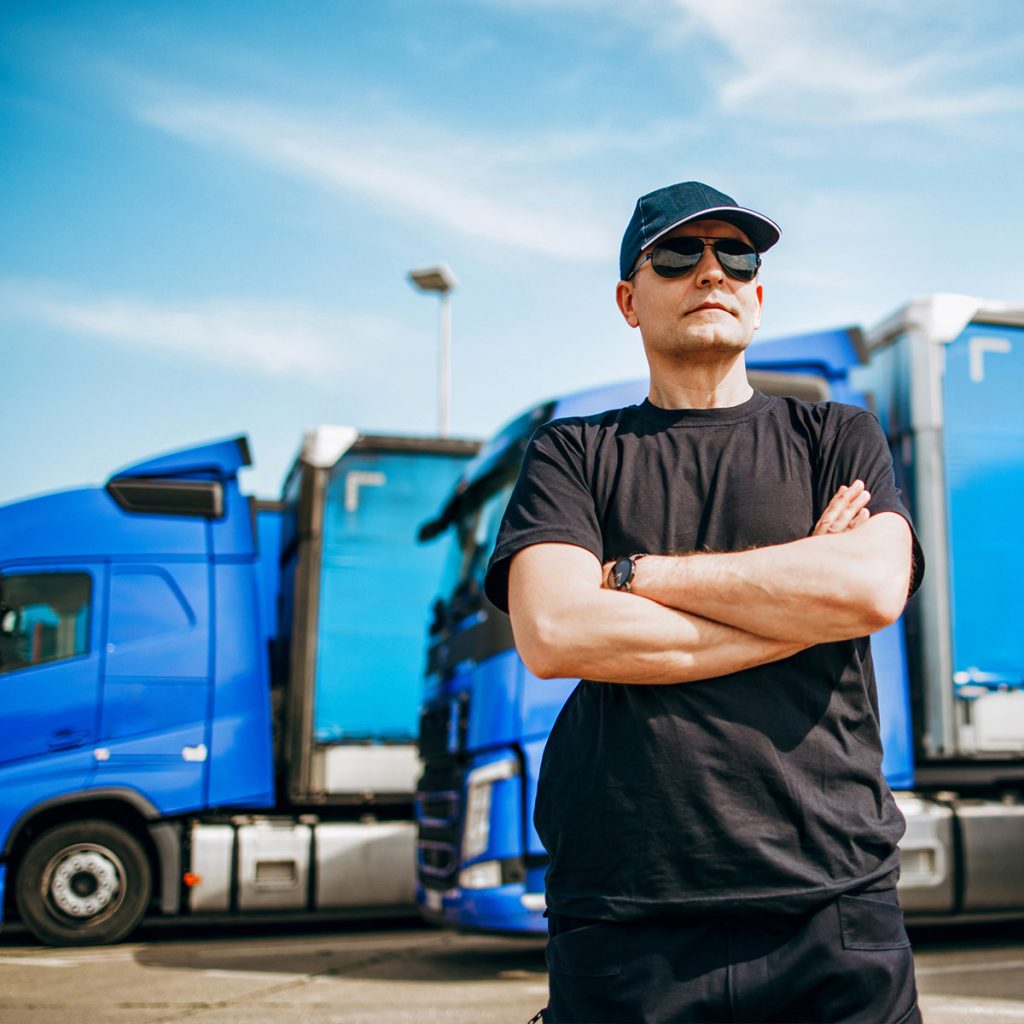 Image of man in hat and sunglasses in front of two blue trucks